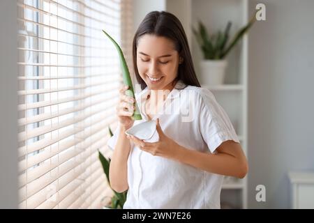 Schöne junge Frau mit einem Teller Aloe Vera Gel in der Nähe des Fensters zu Hause Stockfoto