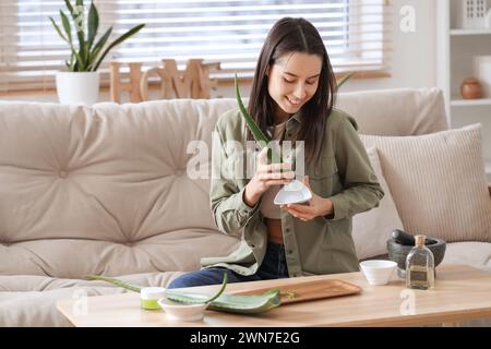 Schöne junge Frau, die Aloe Vera Gel im Wohnzimmer herstellt Stockfoto