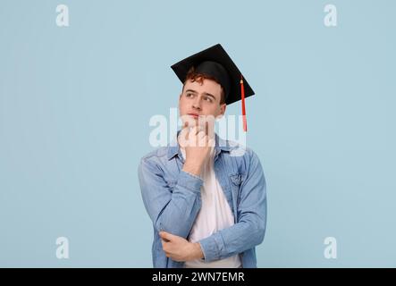 Nachdenklicher männlicher Student in Mörtelplatte auf blauem Hintergrund Stockfoto