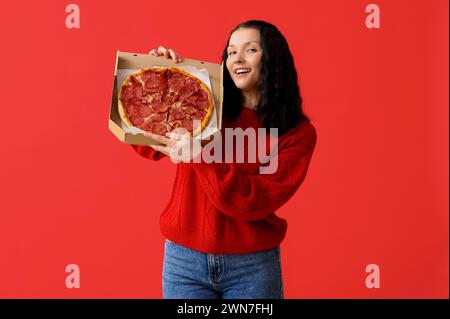 Glückliche junge Frau, die Pappschachtel mit leckerer Pizza auf rotem Hintergrund hält Stockfoto