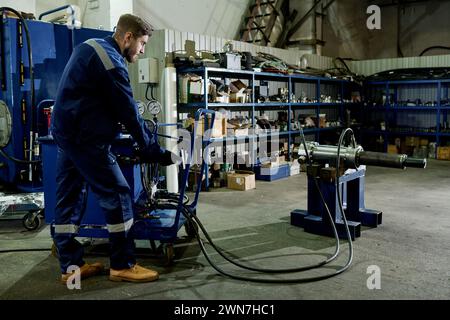 Lange Aufnahme eines Mannes in blauer Uniform, der mit Industriegeräten in moderner Werkstatt arbeitet Stockfoto