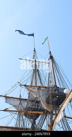 Segeln, Schiff und Mast im Freien mit Flagge für Reisen, Reisen und Abenteuer am blauen Himmel im Sommer. Boot, Holzstange und Vintage-Schonschiff auf einem Stockfoto