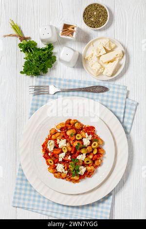 gigantes Plaki, griechische riesige gebackene Bohnen in einer dicken Tomatensauce, bestreut mit Fetakäse, Oliven und frischer Petersilie auf einem Teller mit Zutaten auf Weißwein Stockfoto