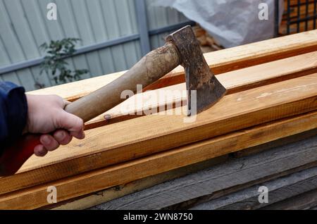 Mann mit Axt. Axt in der Hand. Ein starker Mann hält eine Axt in den Händen vor dem Hintergrund von Feuerholz. Selektiver Fokus, unscharfer Hintergrund Stockfoto