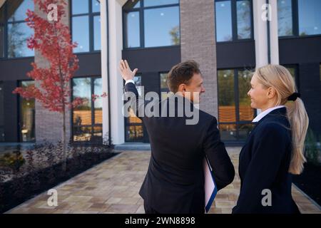 Makler steht in der Nähe des Gebäudes und zeigt es dem Kunden Stockfoto