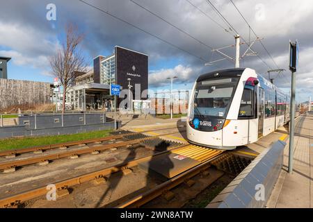 Eine Straßenbahn am Bahnhof Edinburgh Park mit dem Bahnhof Edinburgh Park im Hintergrund. Stockfoto