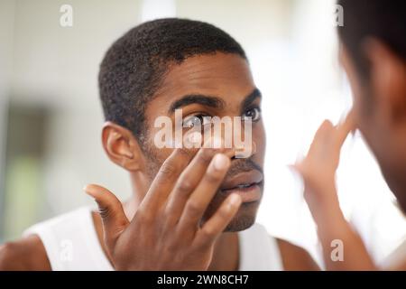 Gesicht, Hautpflege und Lotion mit schwarzem Mann im Badezimmerspiegel von zu Hause, um Anti-Aging-Behandlung anzuwenden. Schönheit, Creme und Kosmetik mit Reflexion junger Menschen Stockfoto