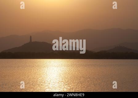 Sonnenuntergang am Kunming See, Sommerpalast, Peking, China, mit Bergsilhouetten und Wolken. Warmer orangefarbener Himmel spiegelt sich in den Wellen des Sees. Stockfoto