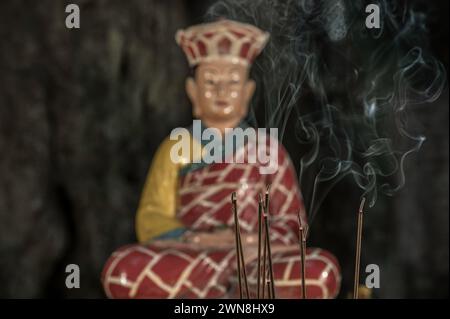 Räucherstäbchen brennen auf einem Alter, vor einer religiösen Statue Stockfoto