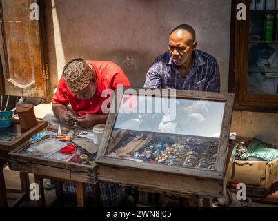 Zwei Männer arbeiten an einem Straßenstand und reparieren und verkaufen Uhren auf dem Stone Town Market in Sansibar, Tansania Stockfoto