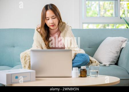 Eine kranke Frau überdeckte die Decke, die an Viren litt, aber immer noch zu Hause mit einem Laptop arbeitet Stockfoto