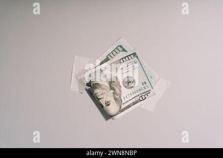100-Dollar-Schein, auf Papierband an einer hellen Wand geklebt Stockfoto