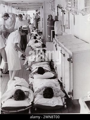 Südchinesisches Meer. Eine Navy Nurse betreut Kranke und Verwundete auf Bahren auf dem Deck des Krankenhausschiffs USS Sanctuary (AH-17), das im Hafen da Nang vor Anker liegt. Die Männer sind gerade mit einem medizinischen Evakuierungshubschrauber an Bord angekommen. Krankenkorps an Bord von Krankenhausschiffen.04/1970; Stockfoto