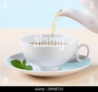 Gießen Sie heißen Tee in eine weiße Tasse mit Pfefferminze Stockfoto