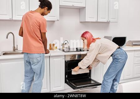 Gut aussehendes fröhliches interrassisches Paar in gemütlichen Haushaltswaren, das zusammen in der Küche zu Hause kocht Stockfoto