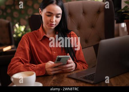 Die Schülerin lernt online auf einem Laptop, bereitet sich auf die Prüfung vor, nutzt Smartphone-Chats mit Freunden, verbringt freie Zeit im Café Stockfoto