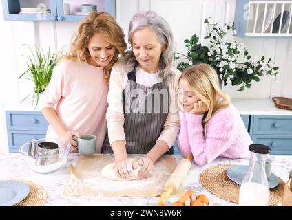 In der gemütlichen Küche arbeiten Oma, Mutter und Enkelin im Team und kneten Teig für hausgemachte Leckereien, Kuchen oder Pizza. Konzept der Verbindung von Generationen von Stockfoto