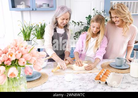 Oma und Mutter bringen Enkelkindern bei, in der Küche mit Mehl und Eiern Teig zu machen. Konzept der Vernetzung von Generationen von Frauen durch Kochen Stockfoto