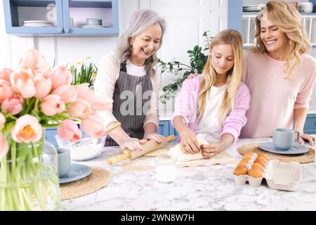 Drei Generationen von Frauen versammeln sich in der gemütlichen Küche, machen und Rollen Teig zusammen mit Lächeln und Lachen aus. Großmutter unterrichtet ihre Tochter und g Stockfoto
