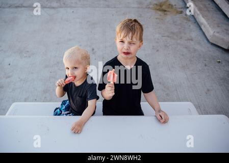 Zwei Jungs essen im Sommer kalte Eiszapfen auf Picknicktisch. Stockfoto