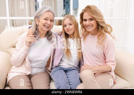 Ältere Frau, ihre Tochter und Enkelin sitzen auf dem Sofa und umarmen sich während des Familientreffens. Drei Generationen von Frauen Stockfoto