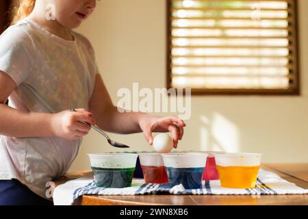 Kleines Mädchen färbt Ostereier am Küchentisch Stockfoto