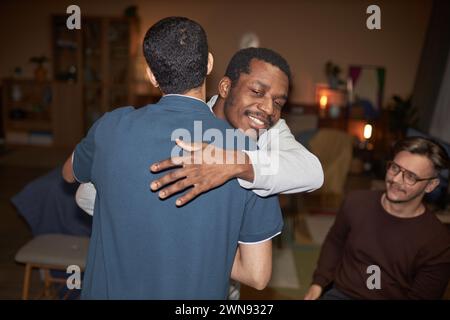 Taille hoch von zwei afroamerikanischen erwachsenen Männern, die sich gegenseitig für eine Hausparty begrüßen, die mit Blitz geschossen wurde Stockfoto