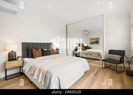 Ein Schlafzimmer mit Stuhl, Bett und großem Spiegel Stockfoto