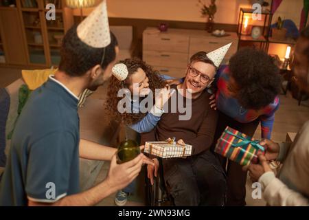 Hochwinkel-Porträt des glücklichen Mannes mit Behinderung feiert Geburtstagsparty mit Gruppe erwachsener Freunde zu Hause Stockfoto