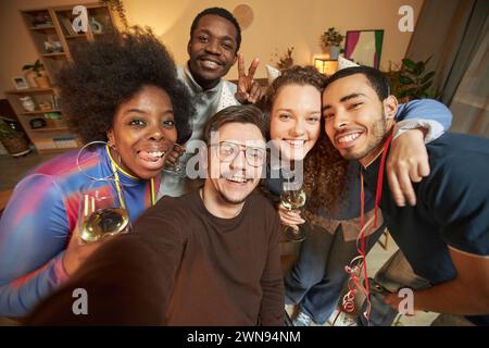 Hochwinkelporträt fröhlicher erwachsener Freunde, die sich zusammendrängen und zu Hause Selfie machen, lächelnd in die Kamera Stockfoto