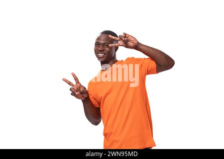Ein junger amerikanischer Typ mit einem kurzen Haarschnitt in einem orangefarbenen T-Shirt zwinkert Stockfoto