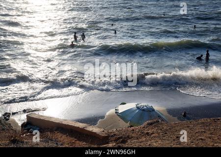 Menschen in Meer und Sonnenschirm am Strand mit Flut kommen in Vouliagmeni Athen Griechenland Stockfoto