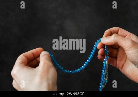 Muslimischer Mann betet blauen Rosenkranz zwischen seinen Händen und betet im Monat Ramadan an an Stockfoto