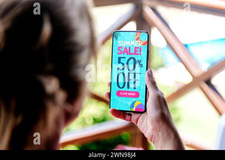 50 % Rabatt auf Sommerangebot. Frau, die ein Mobiltelefon hält, das ein Angebot oder einen Coupon auf dem Bildschirm zeigt. Stockfoto