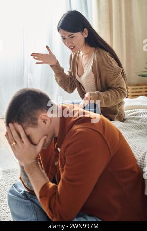 Wütende asiatische Frau streitet sich über Ehemann, der zu Hause mit geneigtem Kopf auf dem Boden sitzt, Scheidungskonzept Stockfoto