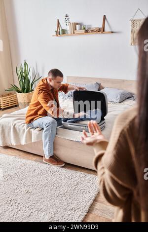 Düsterer tätowierter Mann, der Koffer in der Nähe seiner Frau packt, streitet im Schlafzimmer zu Hause, Missverständnis Stockfoto