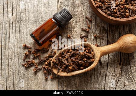 Schließen Sie eine Glasflasche mit ätherischem Nelkenöl und Nelken in Holzschaufel oder Löffel auf Holztisch. Kräuter- und Gewürzöl-Konzept Stockfoto
