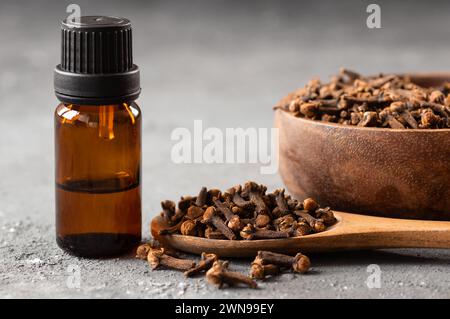 Schließen Sie eine Glasflasche mit ätherischem Nelkenöl und Nelken in Holzschaufel oder Löffel auf Holztisch. Kräuter- und Gewürzöl-Konzept Stockfoto