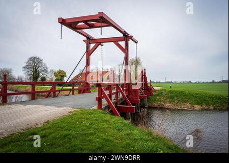 Perspektivische Ansicht einer roten Holzbrücke über einem Graben mit bewölktem Himmel im Hintergrund, Bellingwolde, Groningen, Niederlande Stockfoto