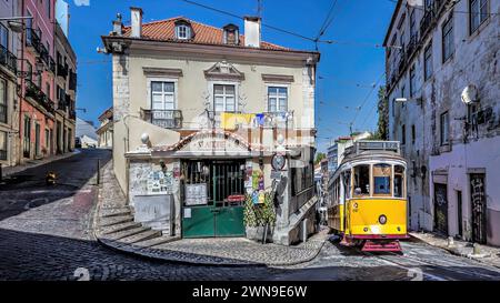 Eine gelbe Straßenbahn auf einer kopfsteingepflasterten Straße, vorbei an einem alten Gebäude unter einem klaren blauen Himmel, Alfama, Lissabon Stockfoto