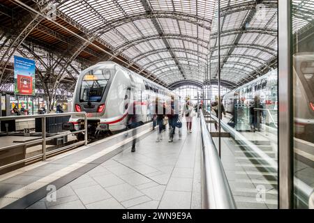 Reisende, die in einer Bahnhofshalle mit beeindruckendem Dach auf Züge warten, Leipzig Hauptbahnhof Stockfoto