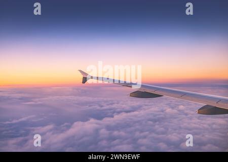 Das Flugzeug fliegt über farbigen Wolken bei Sonnenuntergang oder Sonnenaufgang Wolkenlandschaft, Blick vom Flugzeugfenster aus auf Flügelturbinen und Horizont Stockfoto