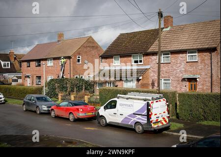 Ein Mitarbeiter von British Telecom/BT OPENREACH, Telekommunikationsingenieur hoch oben auf einer Leiter, die Drähte an einem Haus in Hertfordshire, England, Großbritannien, befestigt Stockfoto