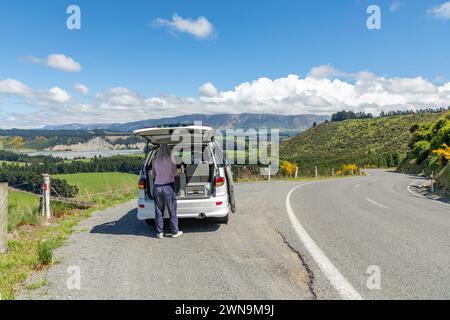 Ein Tourist bereitet einen Snack am Straßenrand mit Blick auf die Rakaia-Schlucht und den Fluss auf der Südinsel Neuseelands in der Nähe von Windwhistle auf der Inland Scenic Route 72 zu Stockfoto