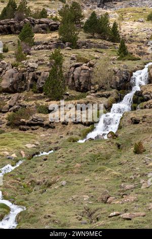 Ruhige Landschaft mit einem kaskadierenden Wasserfall, felsigem Gelände, spärlich grüner Vegetation und bewölktem Himmel Stockfoto