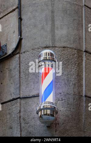 Ein klassischer Friseurmast mit roten, weißen und blauen Streifen, montiert auf einer Steinmauer in einer Straße in Barcelona in Katalonien Spanien Stockfoto