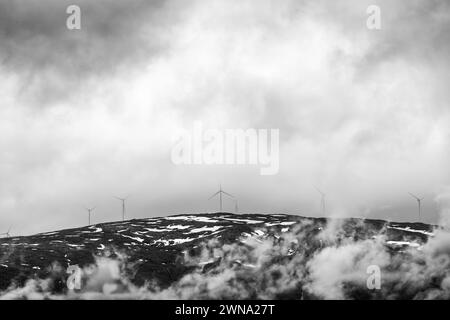 In einem Spiel von Schatten und Licht stehen die Silhouetten der Windräder auf einem norwegischen Kamm und durchdringen die wirbelnden Nebel Stockfoto