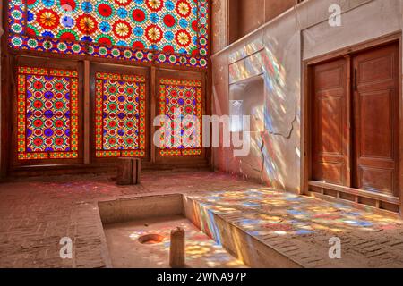 Reich verzierte Buntglasfenster projizieren bunte Lichtspritzer auf Wand und Boden des Pavillons. Dowlatabad Garden, Yazd, Iran. Stockfoto