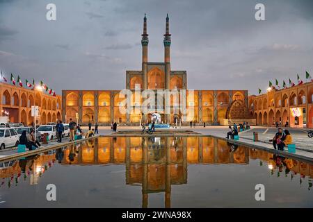 Blick auf den Amir Chakhmaq Komplex und den angrenzenden Wasserpool, beleuchtet in der Abenddämmerung. Yazd, Iran. Stockfoto