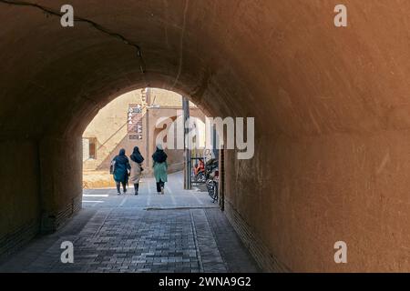 Drei einheimische Frauen laufen zusammen in einer engen Straße in der Altstadt von Yazd, Iran. Stockfoto